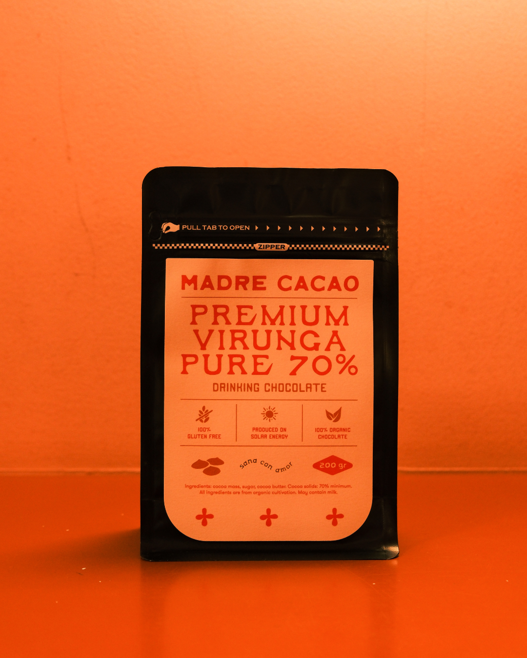 Paket proizvoda Madre Cacao – Premium Virunga Pure 70% Drinking Chocolate od 200g, u crnoj ambalaži sa bež i crvenom etiketom, fotografisan na toploj narandžastoj pozadini. Organska single-origin čokolada iz Virunge, namenjena za pripremu luksuznog toplog napitka.