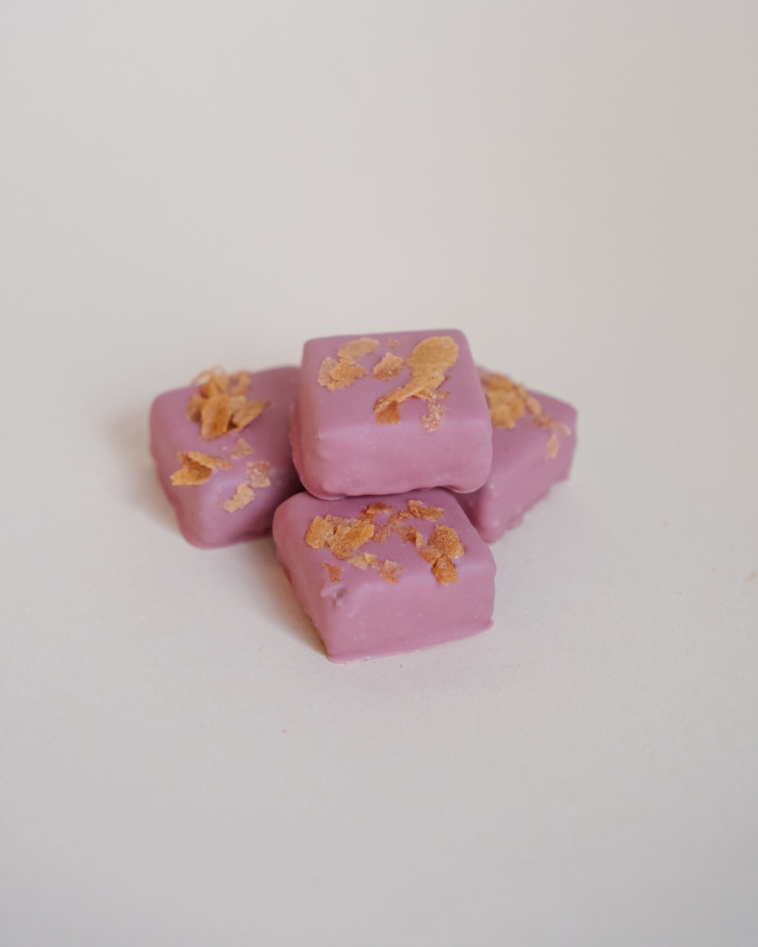 Grupa ružičastih ruby pralina sa zlatnim mrvicama na vrhu, prikazane na neutralnoj pozadini.