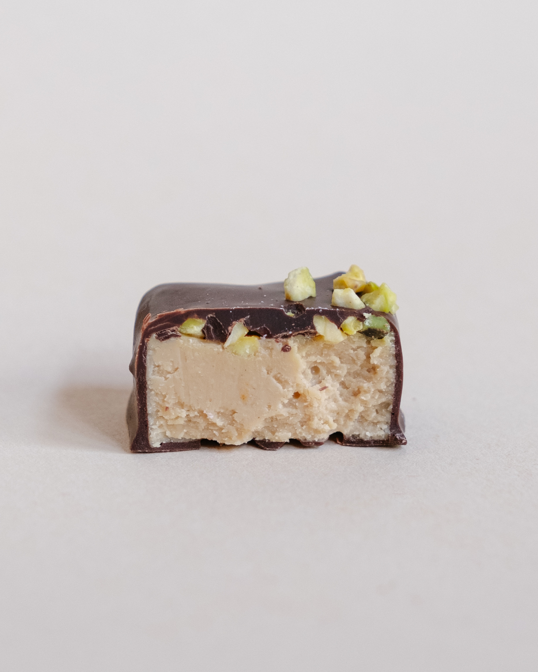 Presek praline od crne čokolade sa tahini kremom i pistaćima – vidi se glatka punjenja tekstura i komadići pistaća