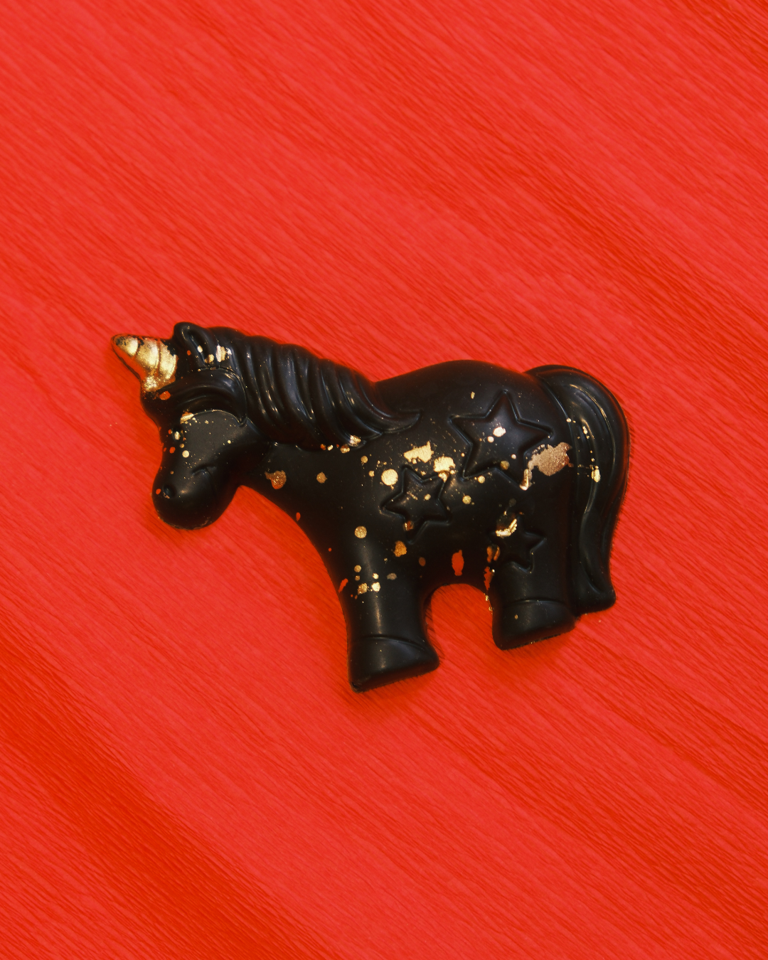 Jednorog od crne čokolade sa jagodom i kikiriki puterom, ručno izrađen, sa zlatnim detaljima.