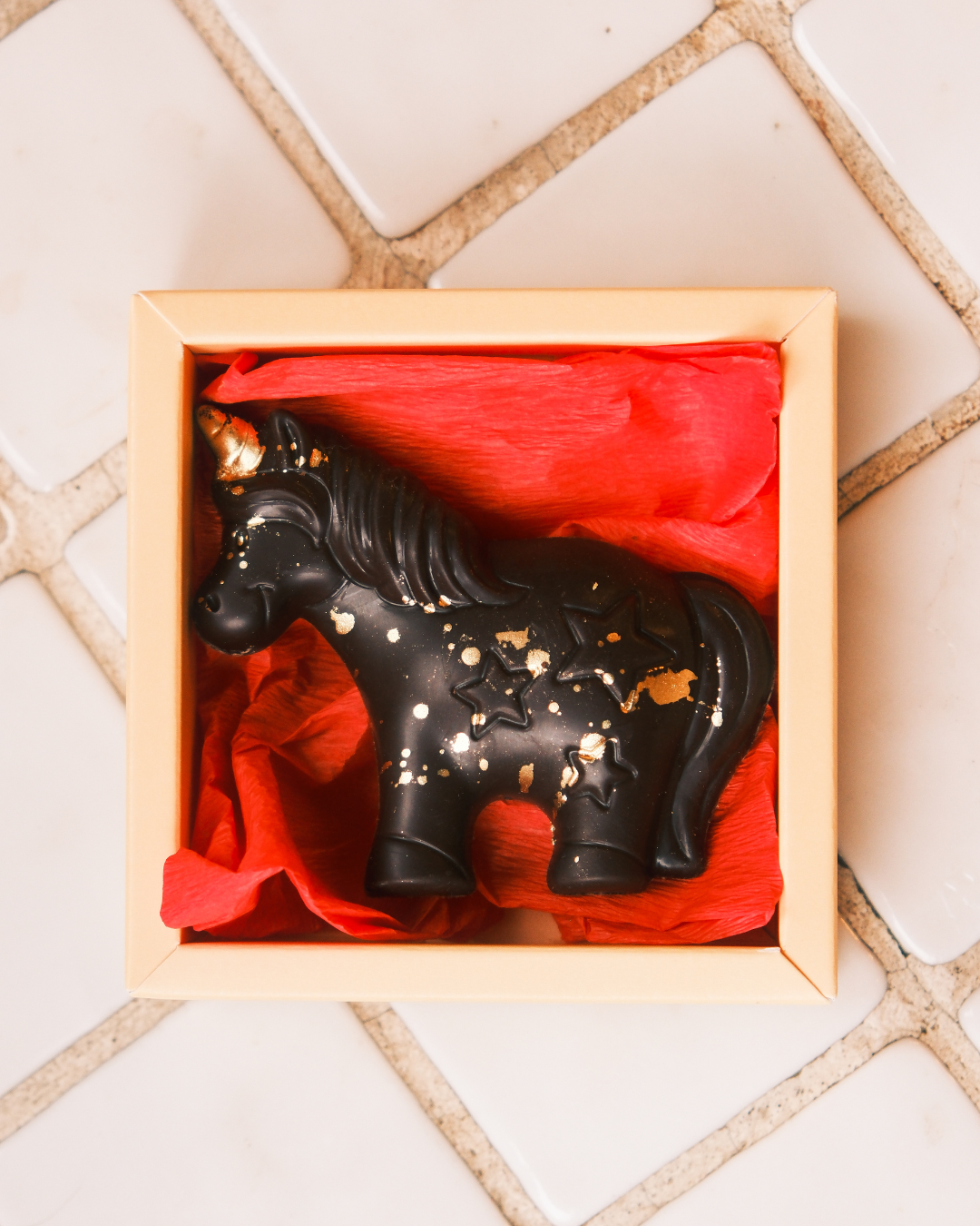 Ručnо rađena čokoladna figura Jednorog od crne čokolade sa jagodom i kikiriki puterom, u poklon pakovanju.