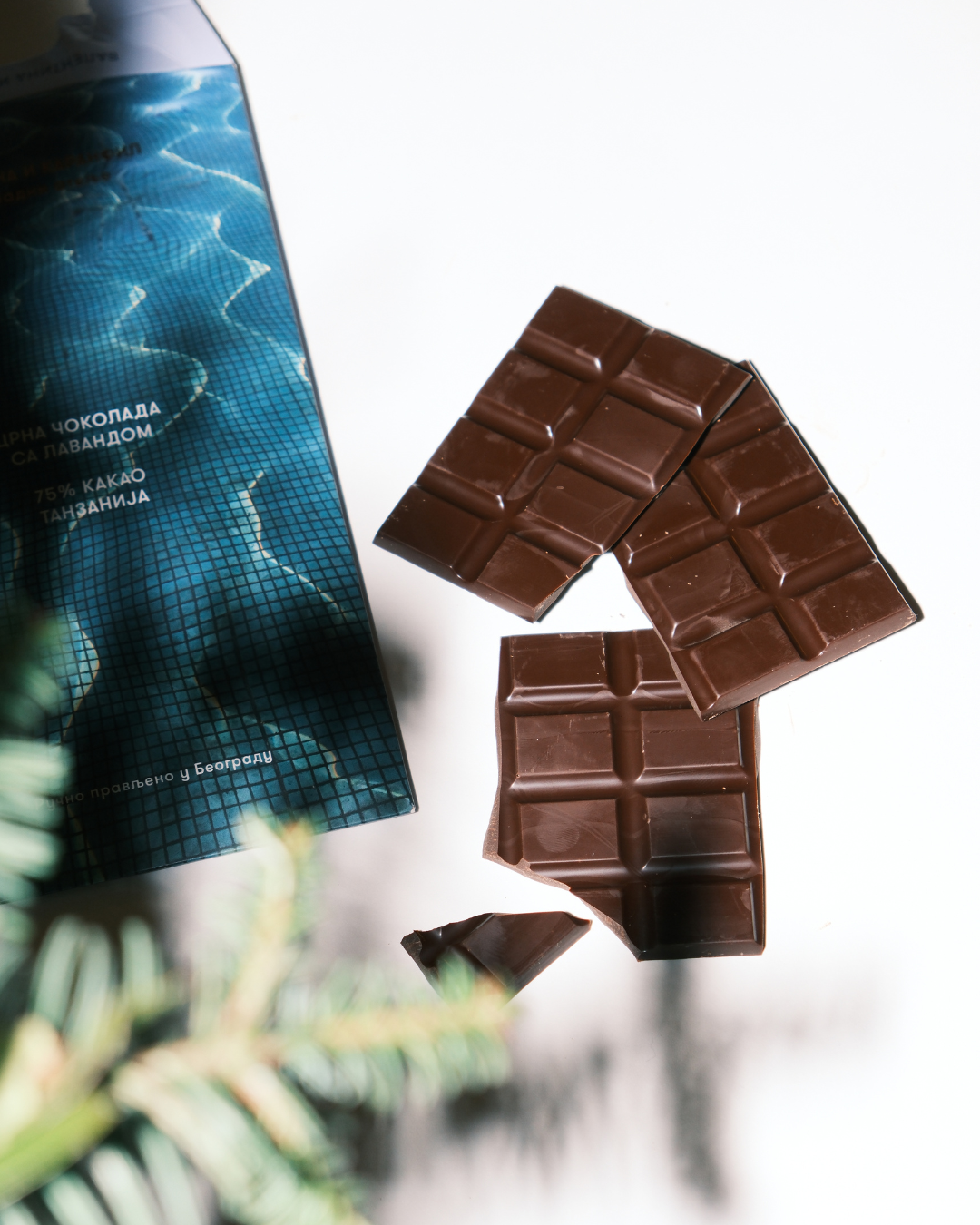 Tabla crne čokolade sa lavandom pored pakovanja Valentina i Karanfil na beloj podlozi, sa senkama grančica.