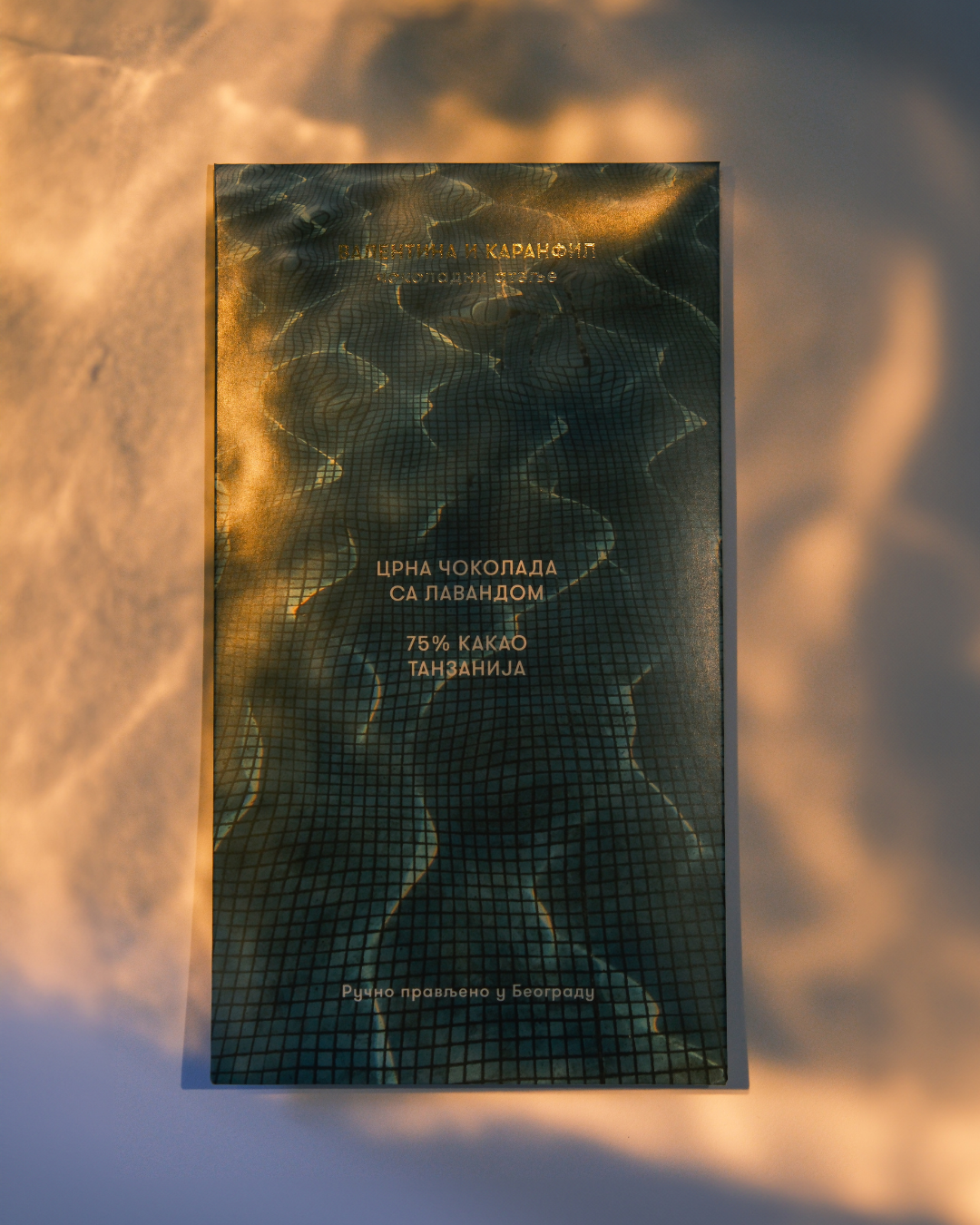 Pakovanje čokolade Valentina i Karanfil osvetljeno toplim svetlom zalaska sunca – motiv vode i refleksije svetlosti.