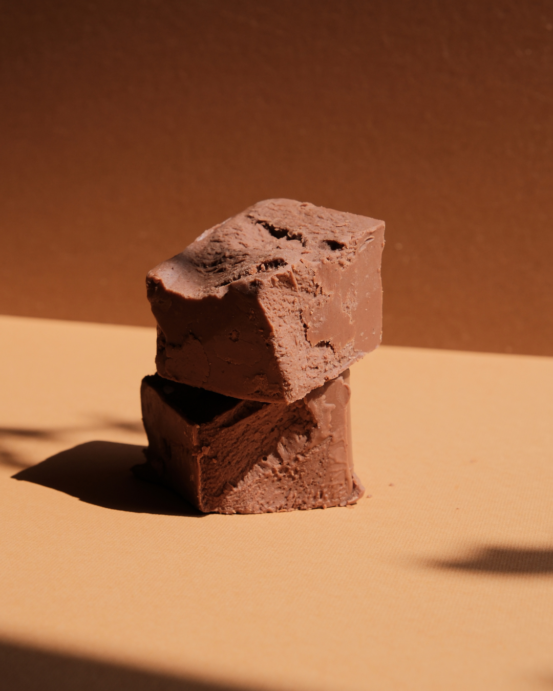 Kocke kremaste đanduje od mlečne čokolade i lešnika na bež pozadini u prirodnom svetlu.