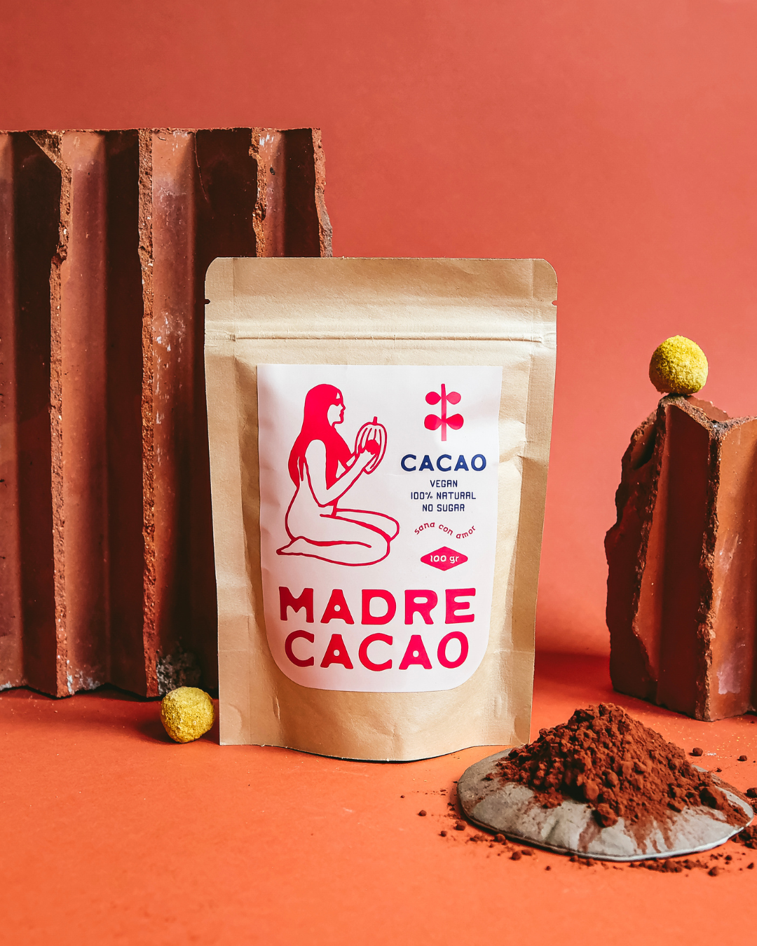 Pakovanje Madre Cacao kakao-praha od 100 g na narandžastoj pozadini, pored nasutog kakao-praha.