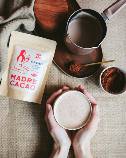 Topli napitak od Madre Cacao kakao-praha u rukama, pored džezve, posude sa kakaom i pakovanja proizvoda.