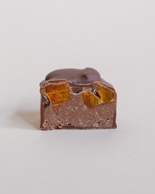 Presečena pralina od mlečne čokolade – vidi se kremasti sloj sa pastom od lešnika i komadićima sušene kajsije.